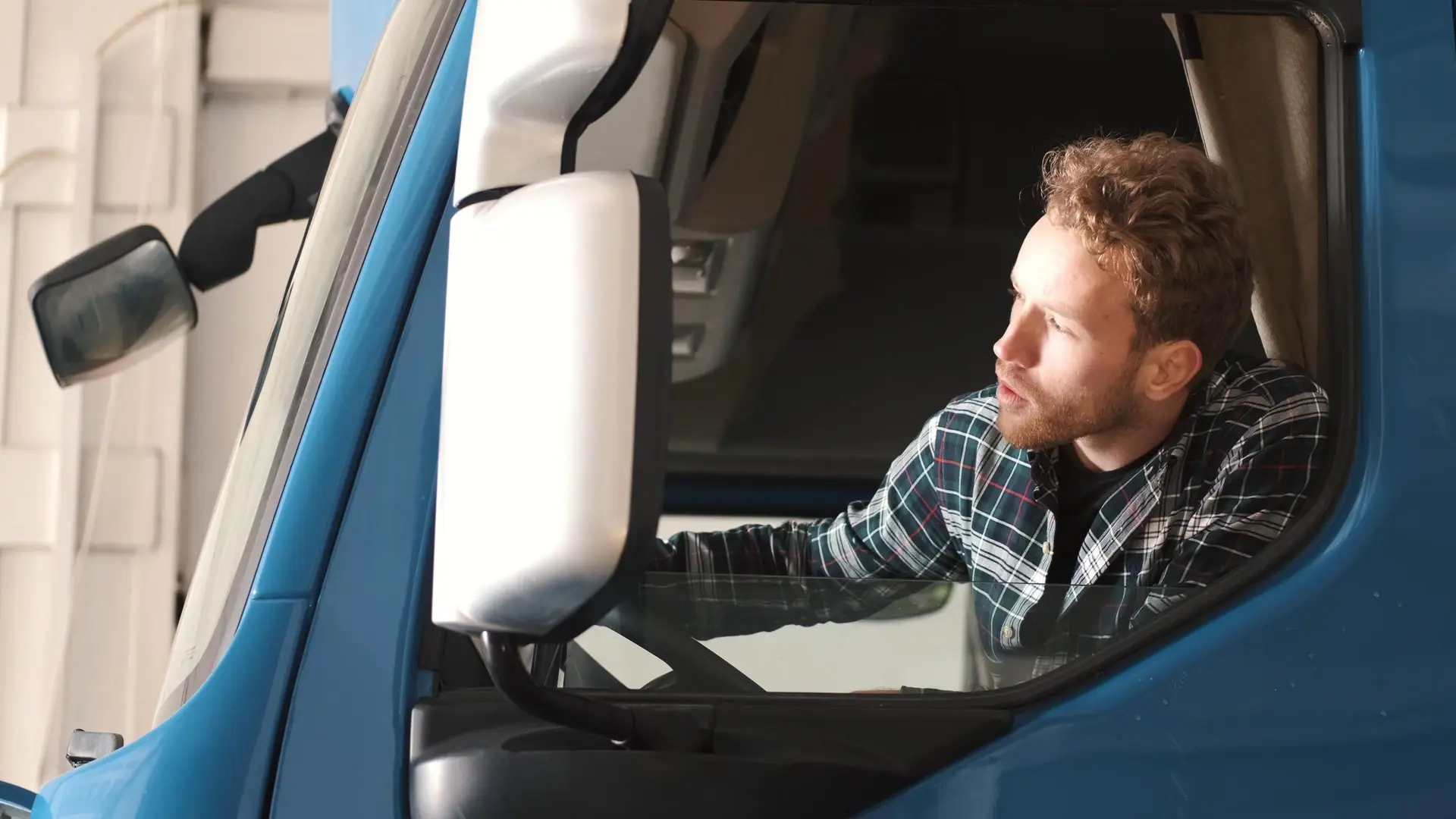 A truck driver in the cab, looking out of the window.